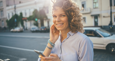lächelnde Frau am Straßenrand mit dem Smartphone in der Hand