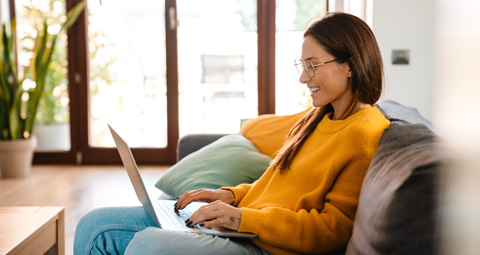 Frau sitzt mit dem Laptop auf dem Sofa und arbeitet